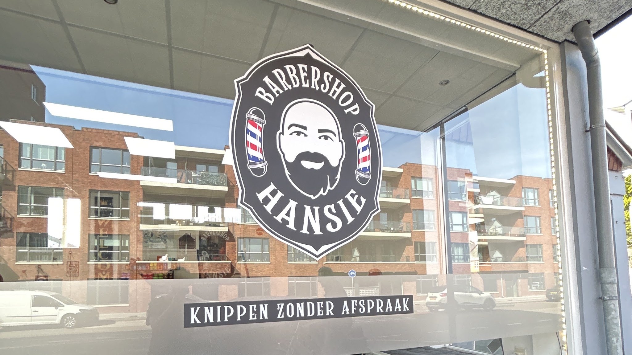 De etalageruit van Barbershop Hansie met het logo en de tekst Knippen zonder afspraak